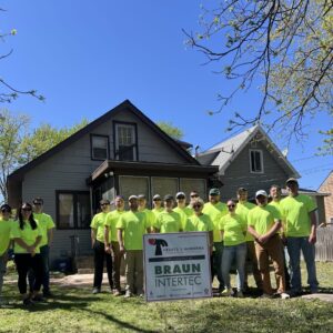 Braun Intertec team members gathered around the front of Camille’s St. Paul home. The team is wearing bright yellow shirts and standing in front of a sign with Hearts & Hammers and Braun Intertec logos.