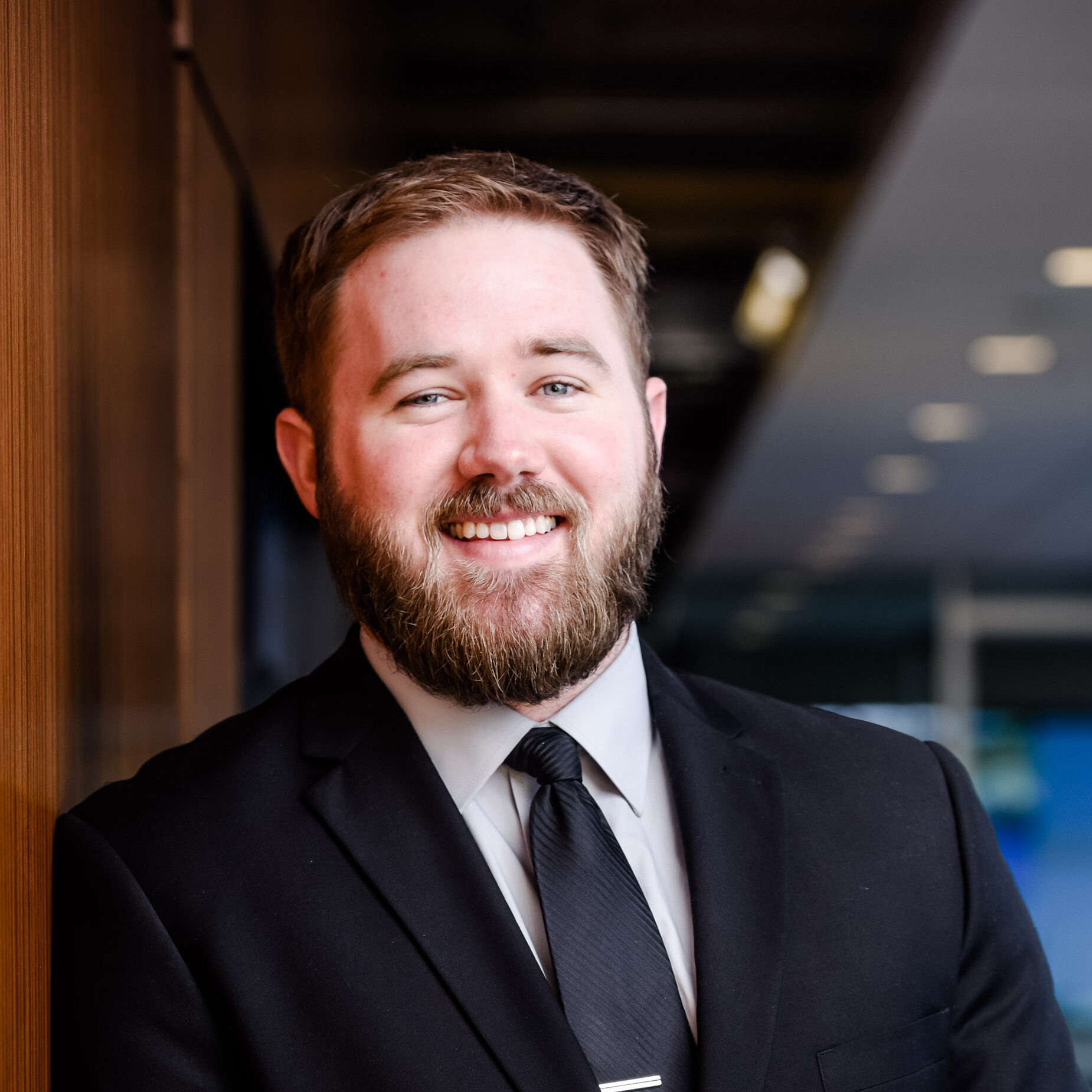 osh Dougherty, a board member of Hearts & Hammers from Mortenson Construction, standing in a professional setting wearing a black suit and tie